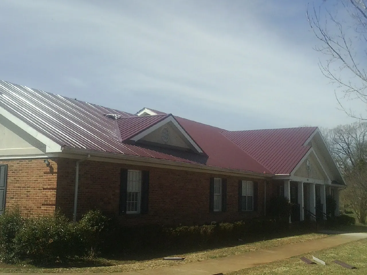 Red metal roof with gabled entries on a long brick building, from a Hail Damage Roof Repair job in Wexford