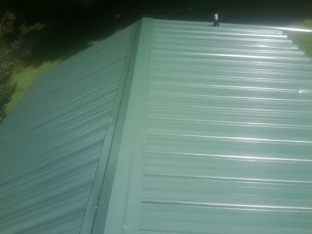 New green metal panels meeting at the ridge of a roof — Flat Roof Repair work by our crew in Wexford