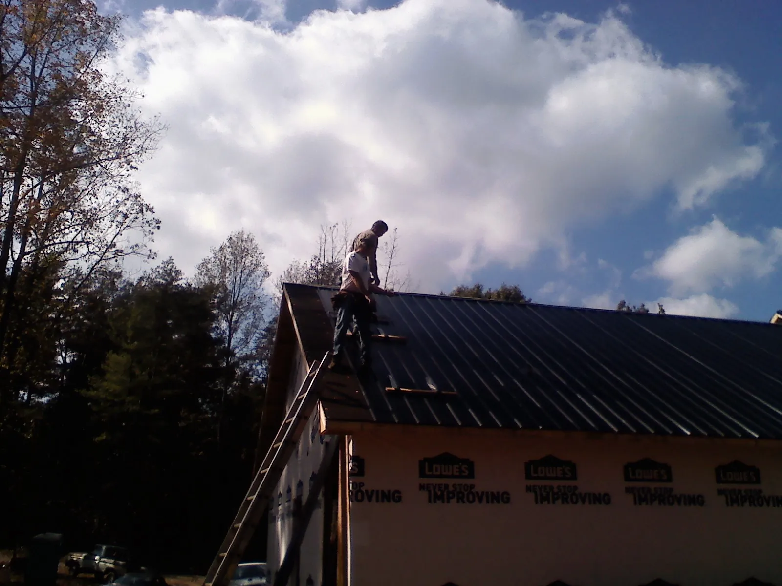 Roofer fastening dark metal panels high against a cloudy sky, from a Roof Inspection job in Wexford