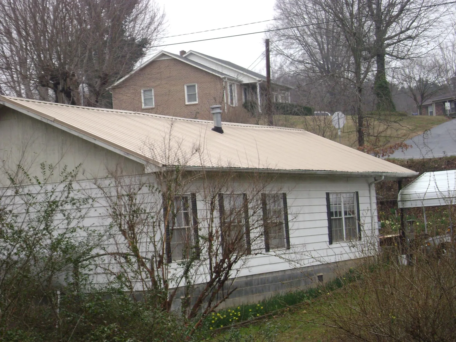 Tan metal roof on a white sided house set into a hillside — Commercial Roofing by Roofing Brothers in Wexford